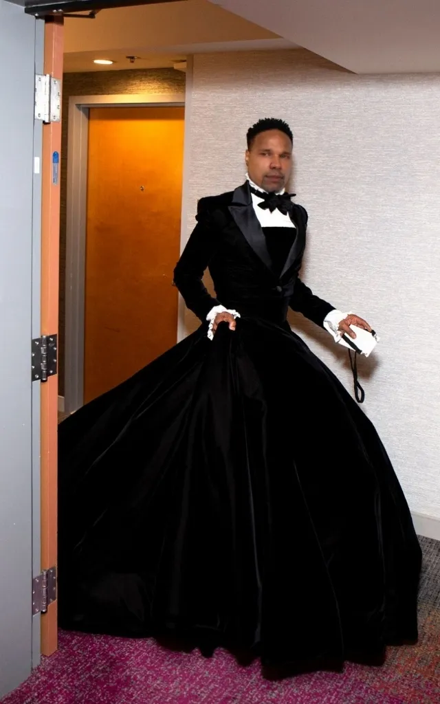 A man in a tuxedo standing in a doorway, shot from a dramatic low angle with high contrast black and white lighting