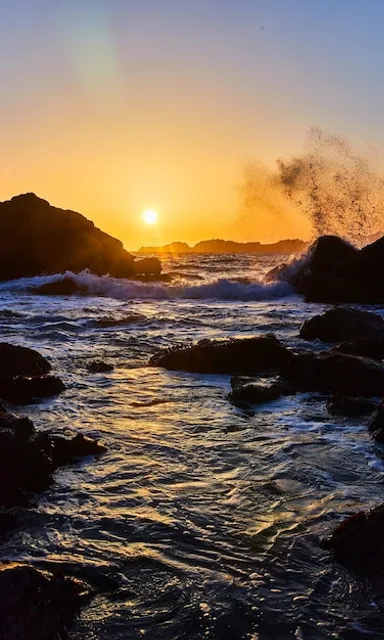 the sun is setting over the ocean and rocks