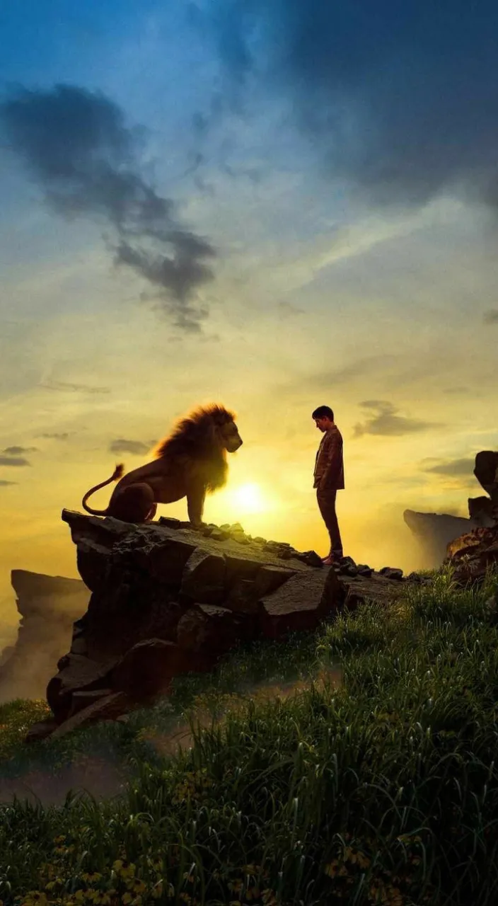 a man standing on top of a cliff next to a lion