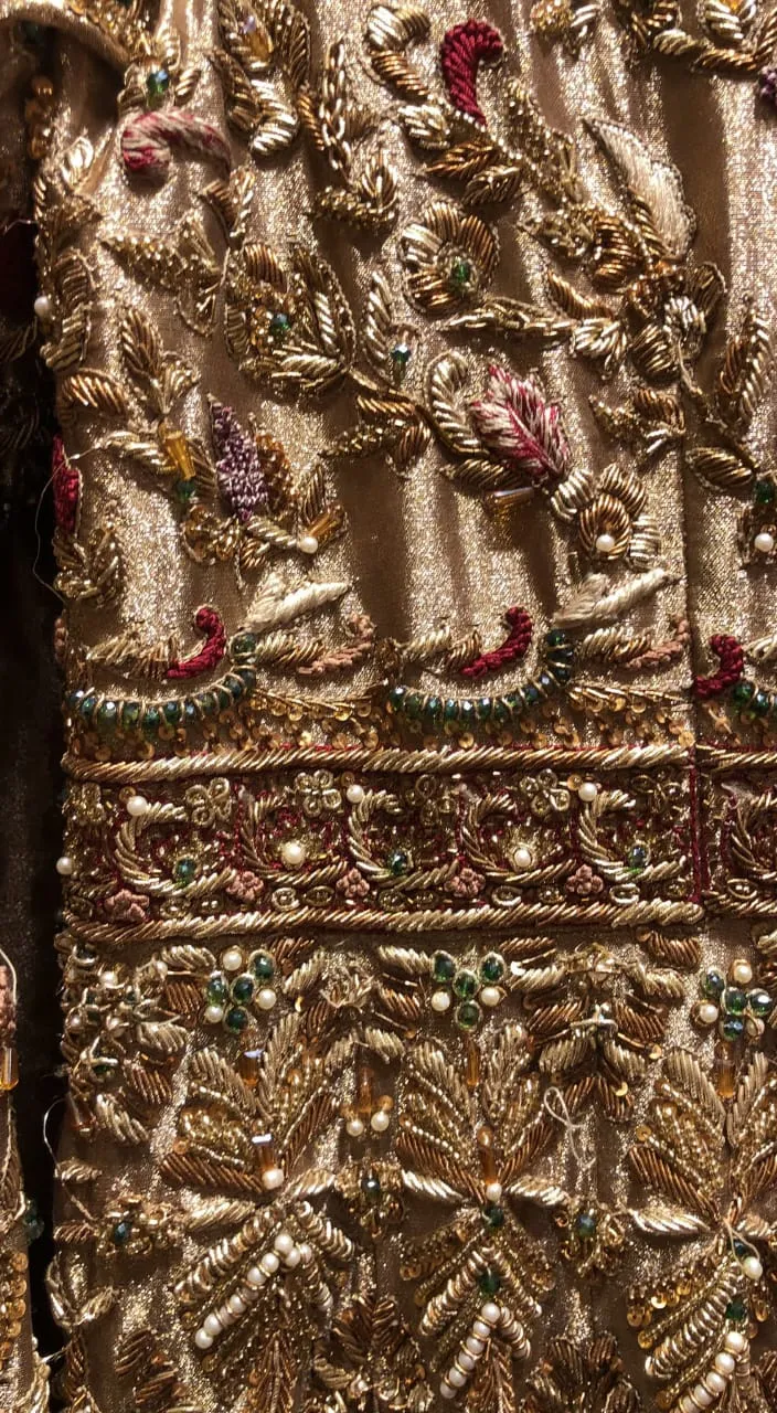 Close up of a gold dress with beads draped over rock at shore, with sunlight reflecting off water in the background