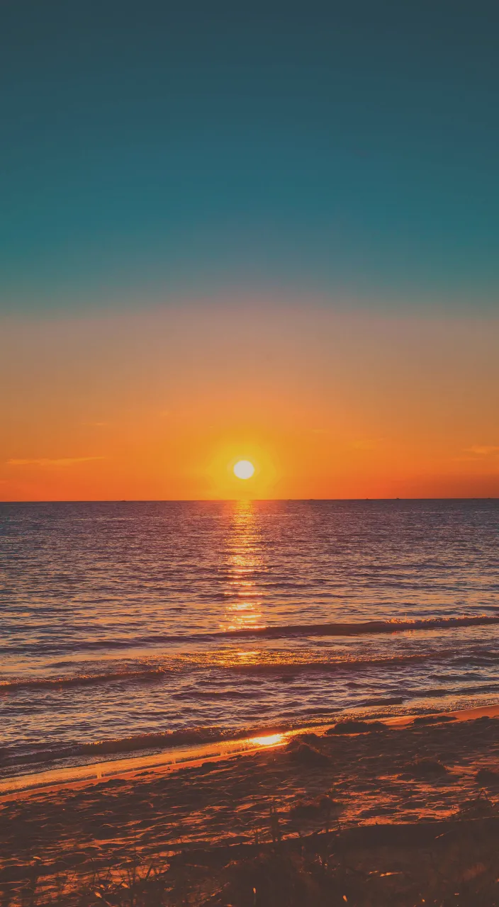 the sun is setting over the ocean on the beach