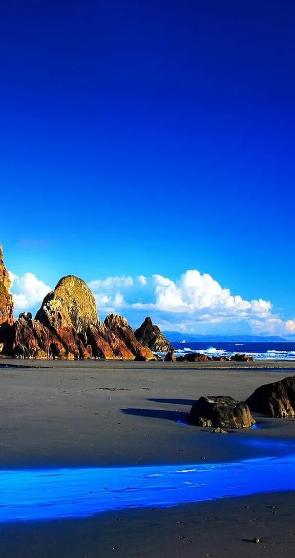 a beach with rocks and blue water on a sunny day