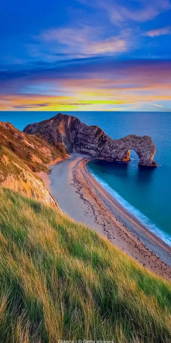 a beautiful sunset at the beach with a rock formation in the water