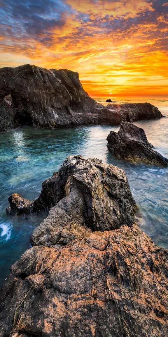 a beautiful sunset over the ocean with rocks